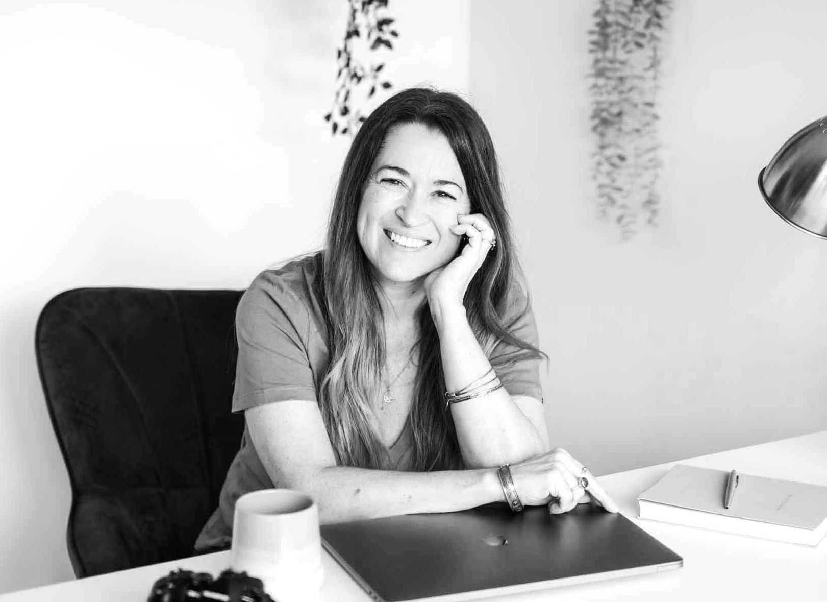 Sarah-Oughton Woman with long hair leaning on her hand at her desk with laptop