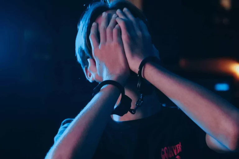 A boy with handcuffs and hands over his face