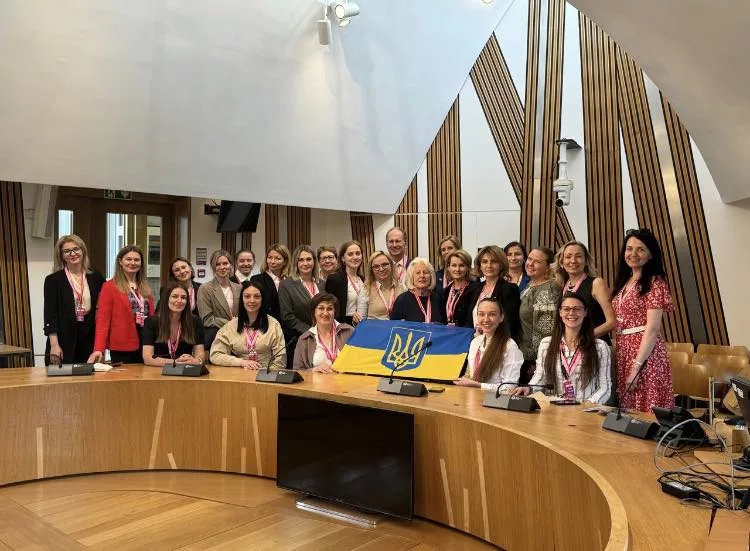 A group of women standing around a curved desk with Ukrainian flag
