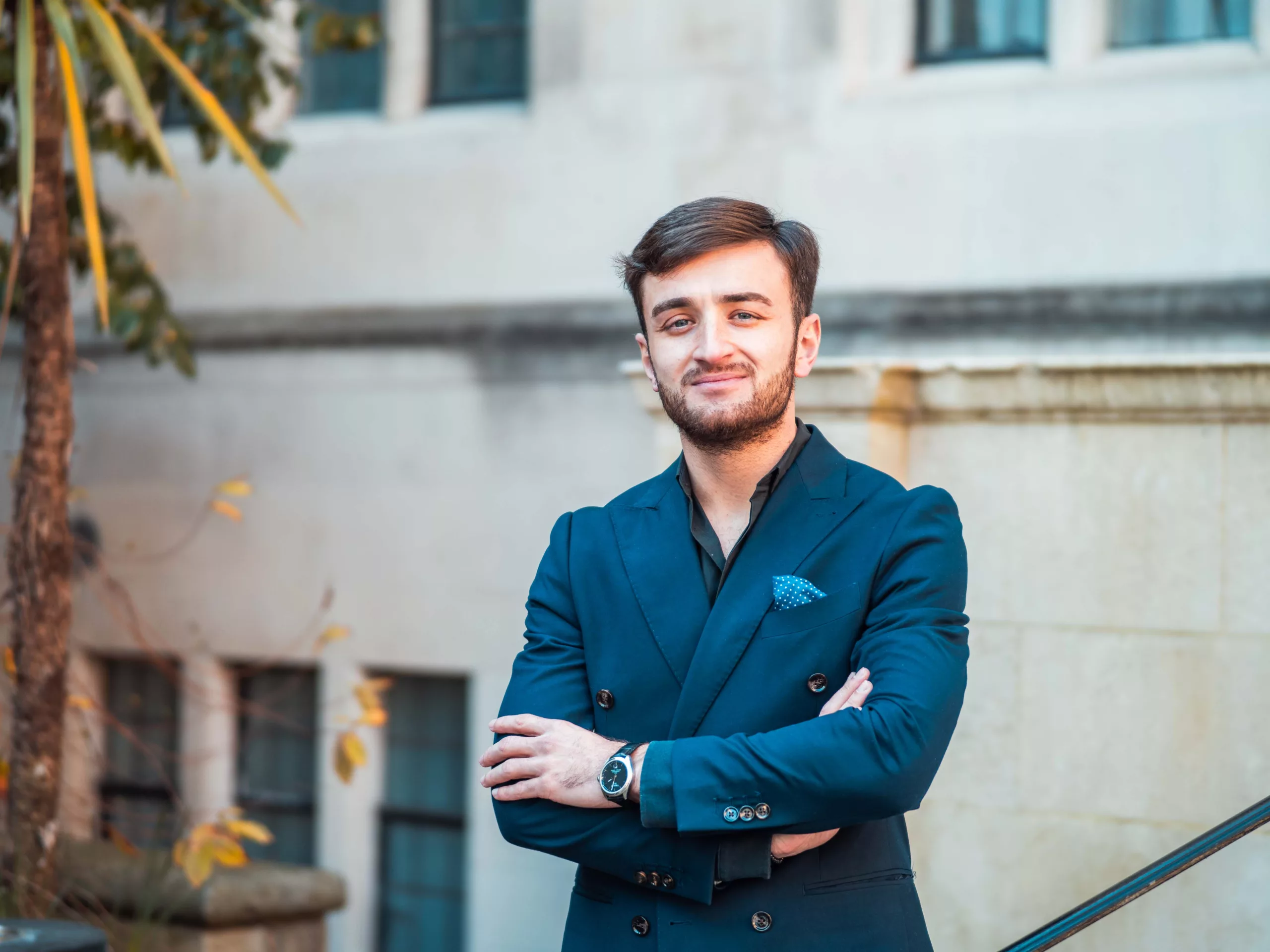 Man in blue suit with arms folded in front of building