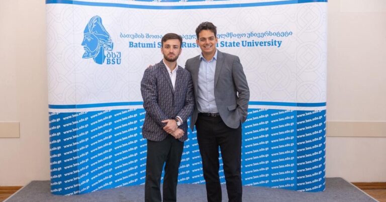 Giga and Dan at a conference in front of a banner