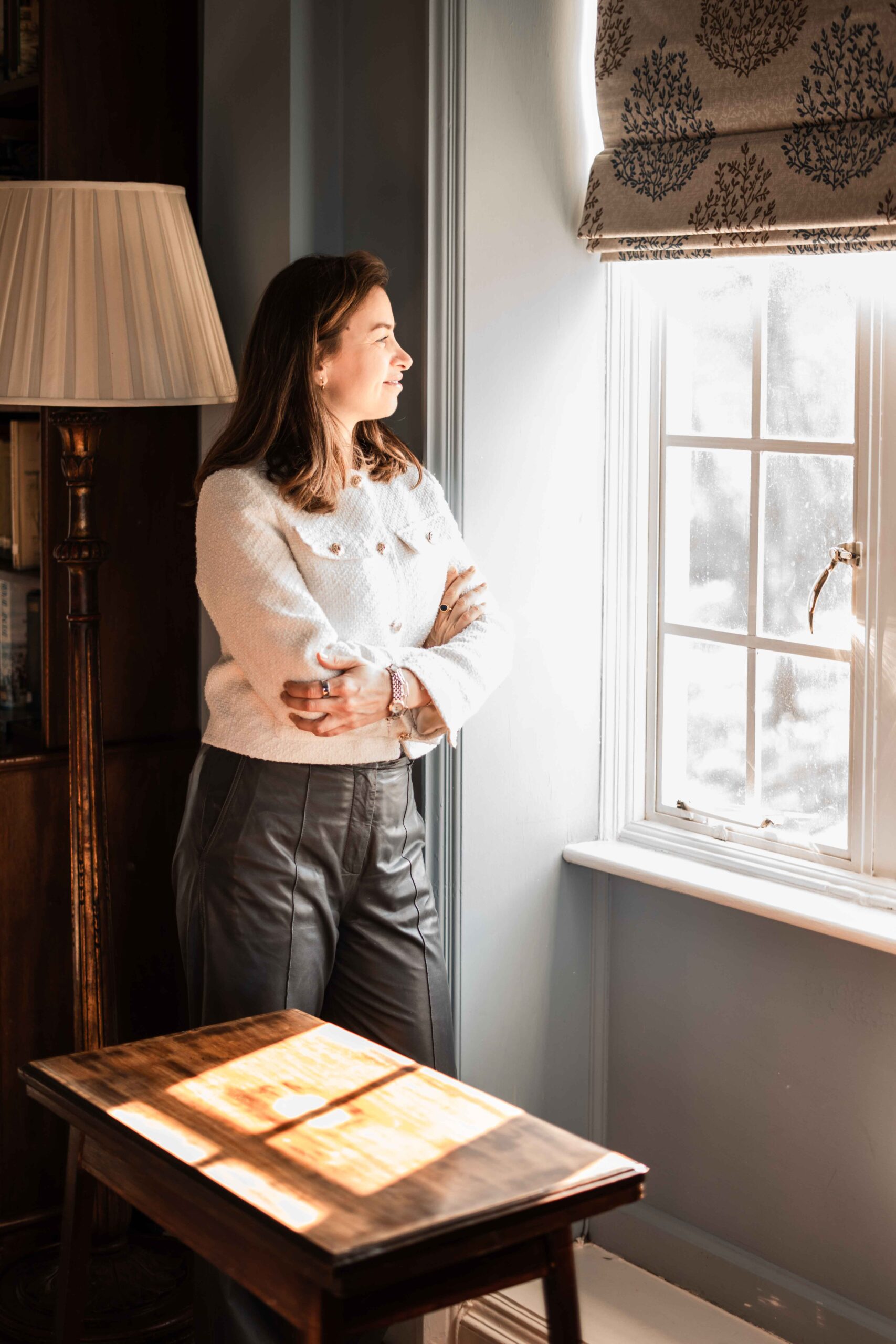 Liliana at Cumberland Lodge A woman leaning against the wall with folded arms and gazing out the window