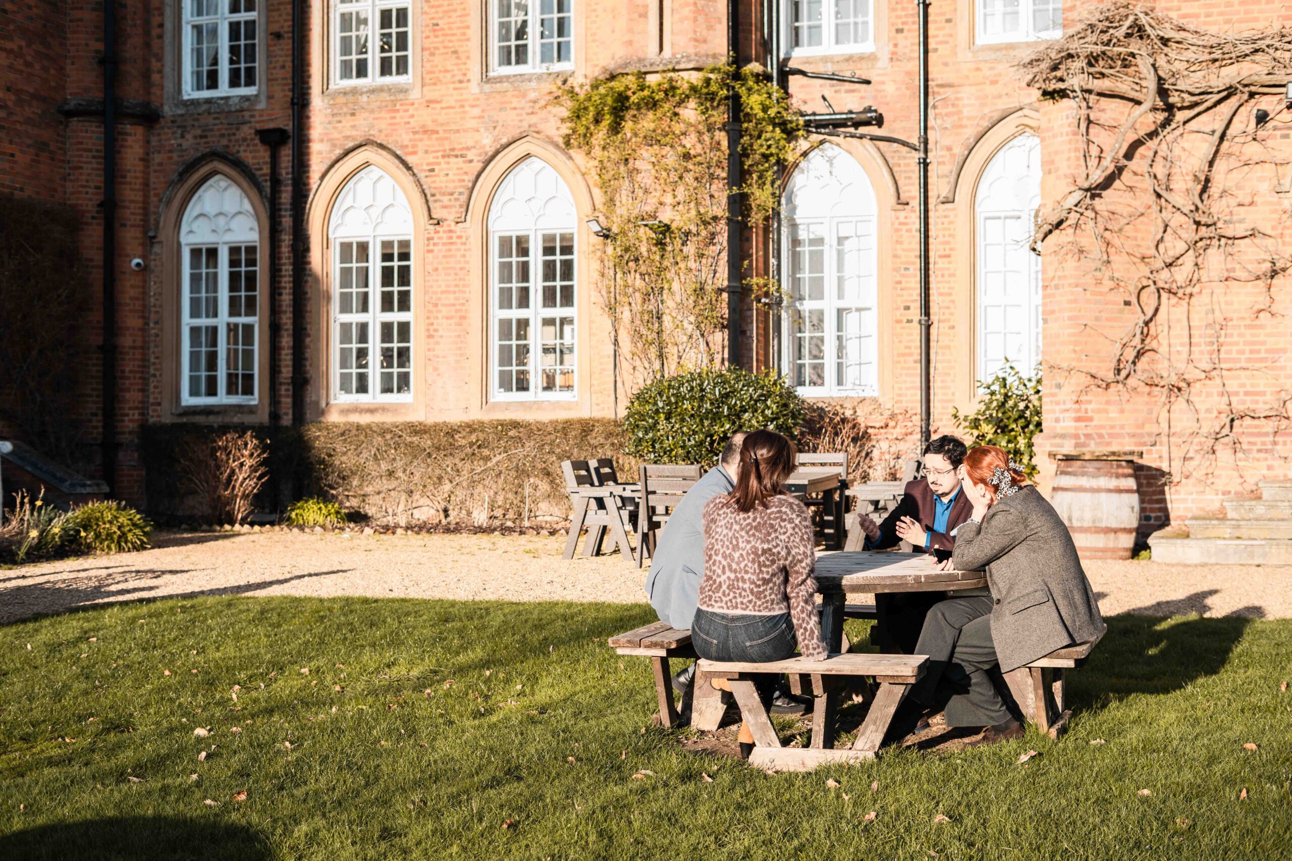 A small group sat talking at a table in front of a grand brick building