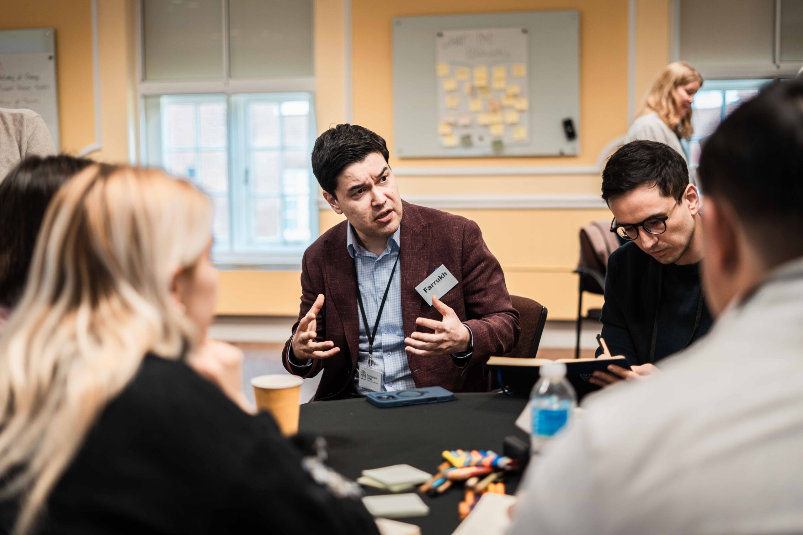 A man sat at a table explaining something to his Fellows