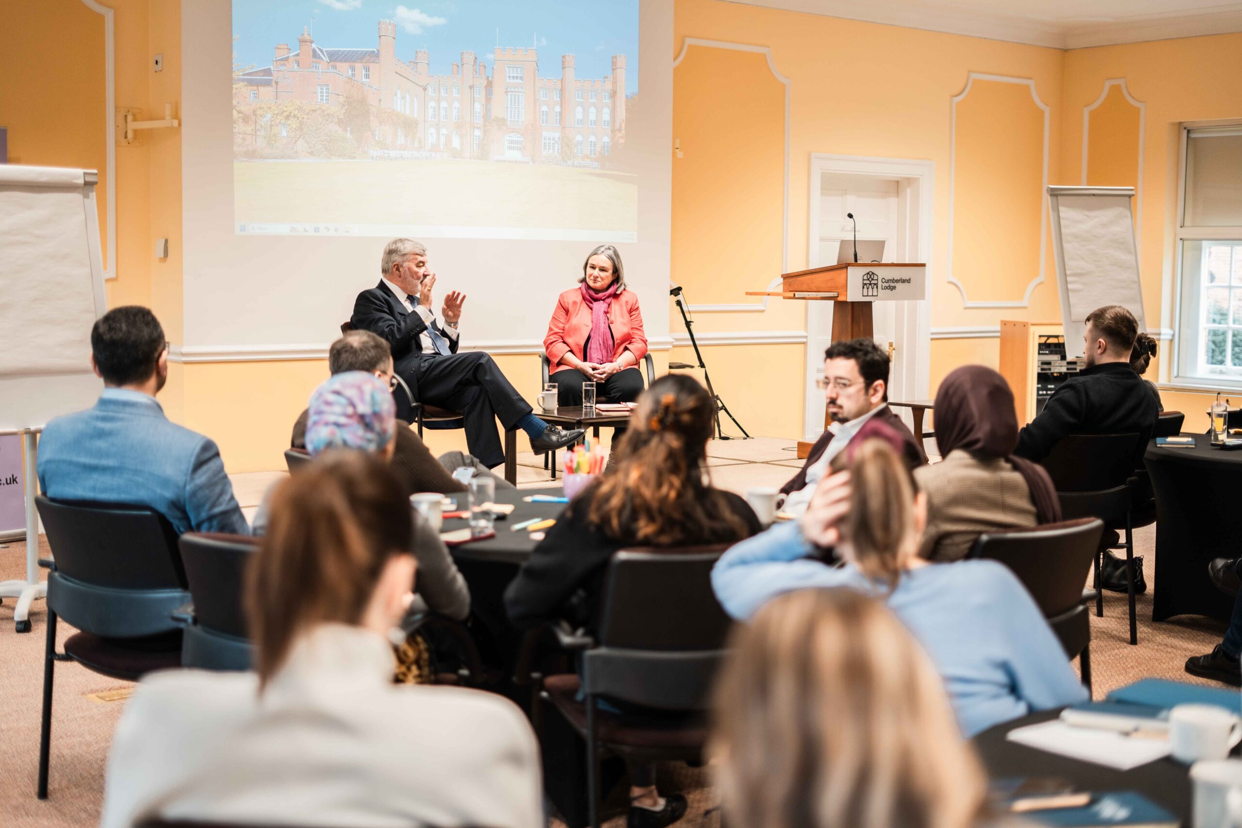 Alison Suttie and John Alderdice in conversation at an Ideas Exchange A man and a woman seated on stage talking to a room full of people