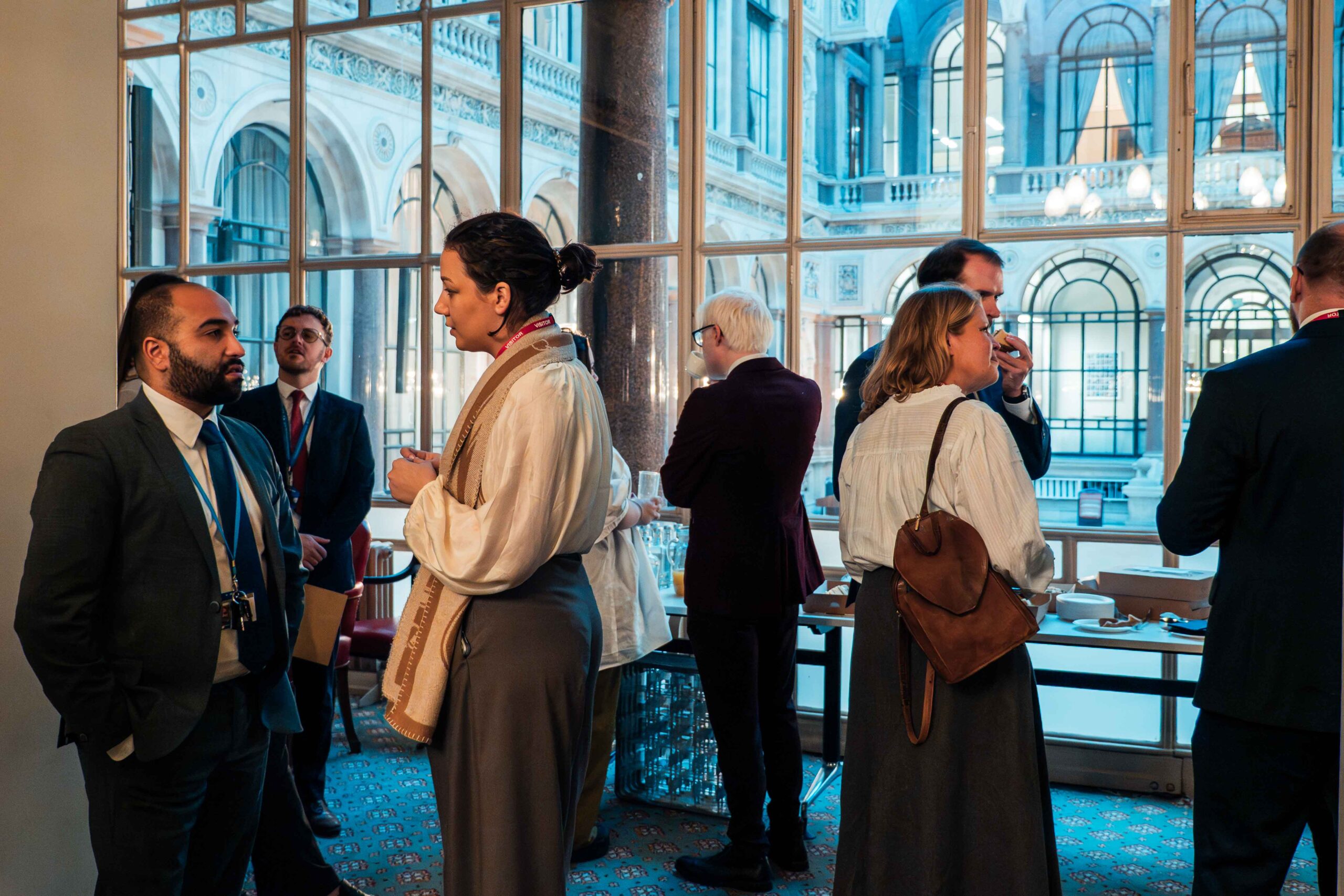 A group of people socialising and networking over tea in a grand room with tall windows