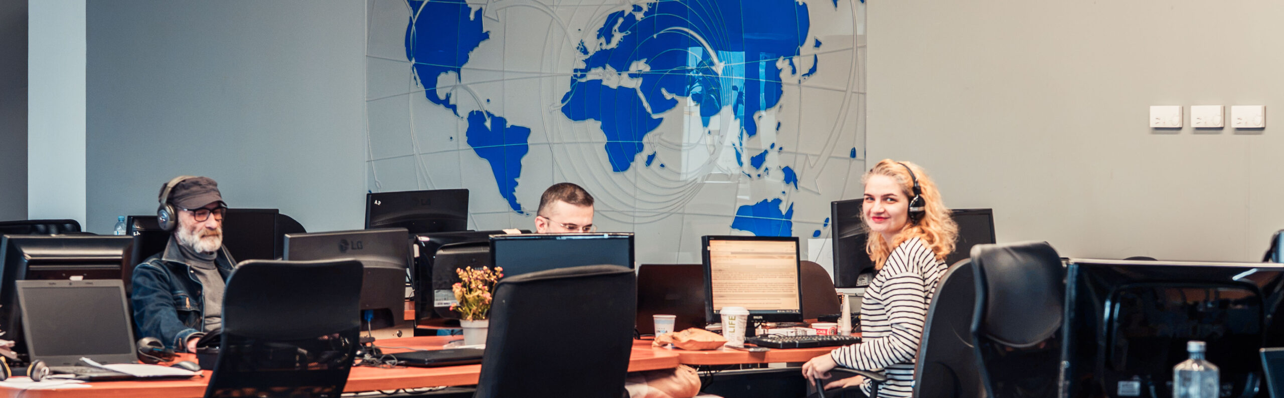 Three people working in a row at computers with a map of the world on the wall