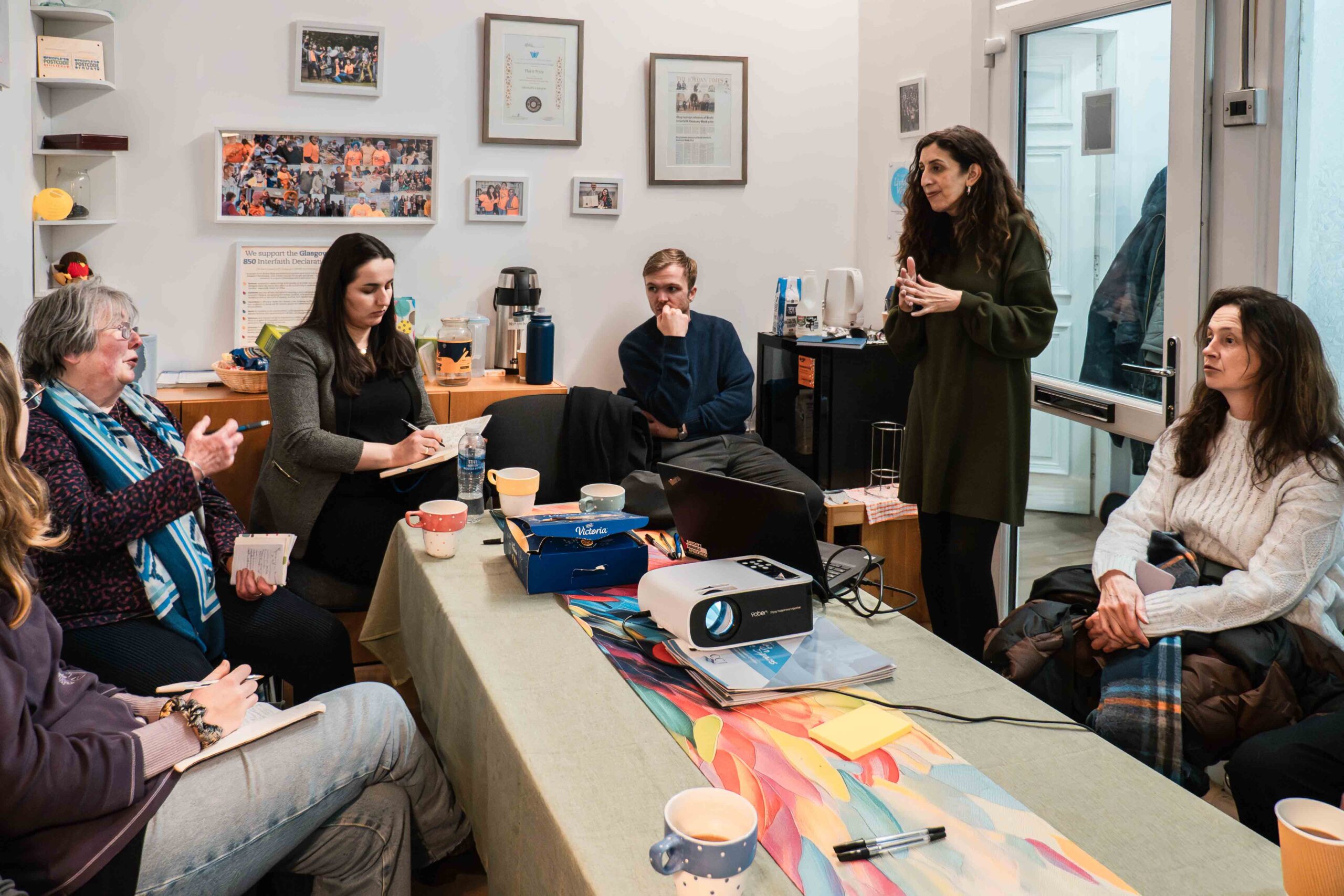 A woman standing in a small room talking to a group of people