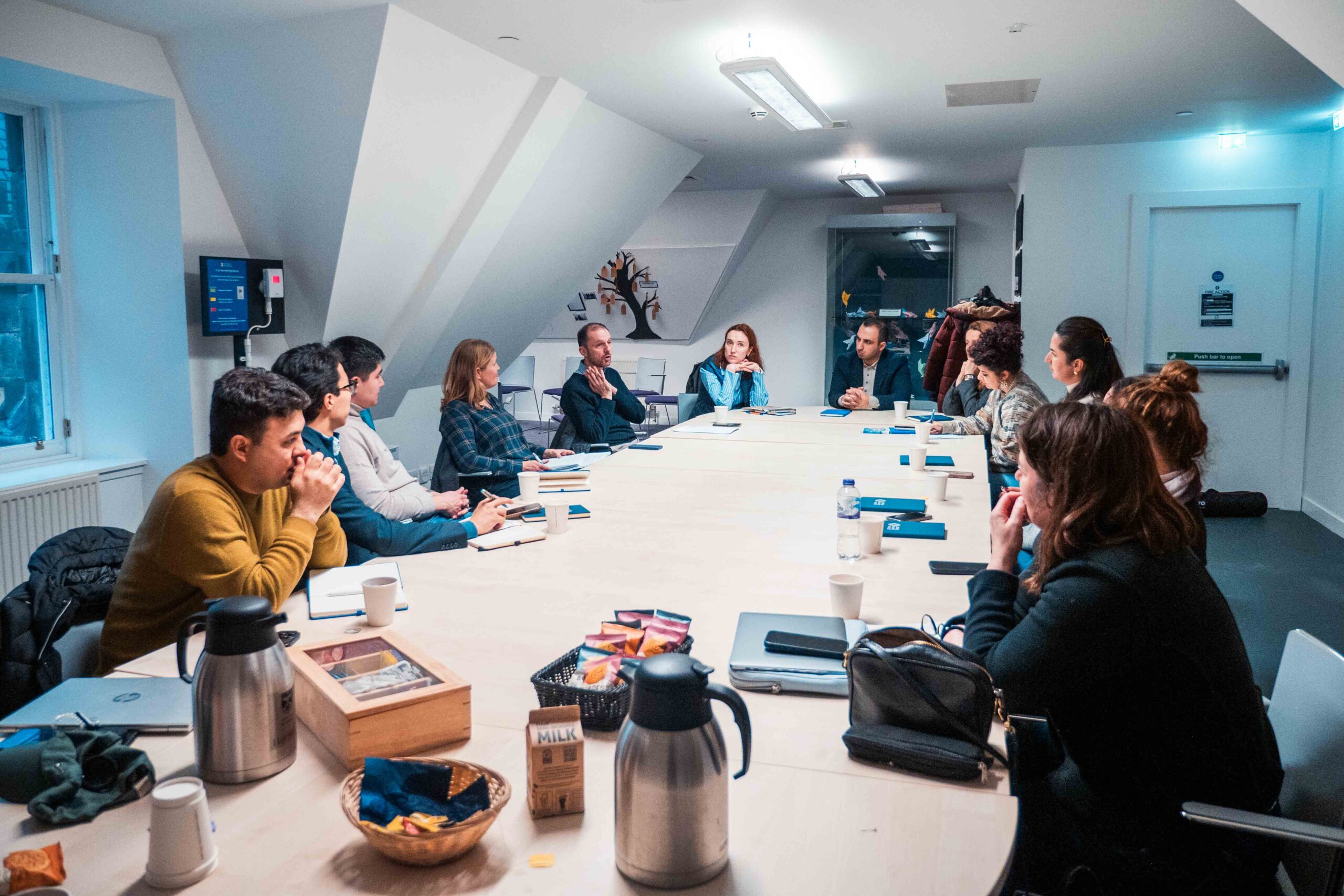Group discussion at st Andrews University A long table in a room with sloped ceiling with 15 people sitting around it