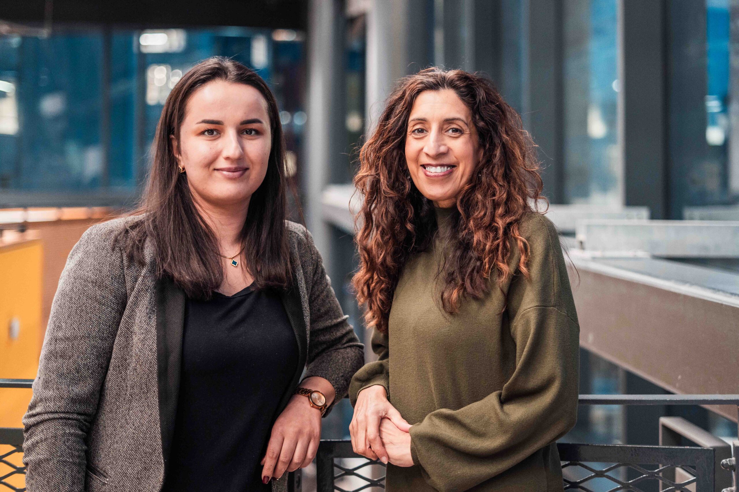 Two women standing inside a building leaning on a handrail and smiling