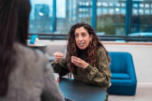 A woman with long hair at table in discussion with another woman