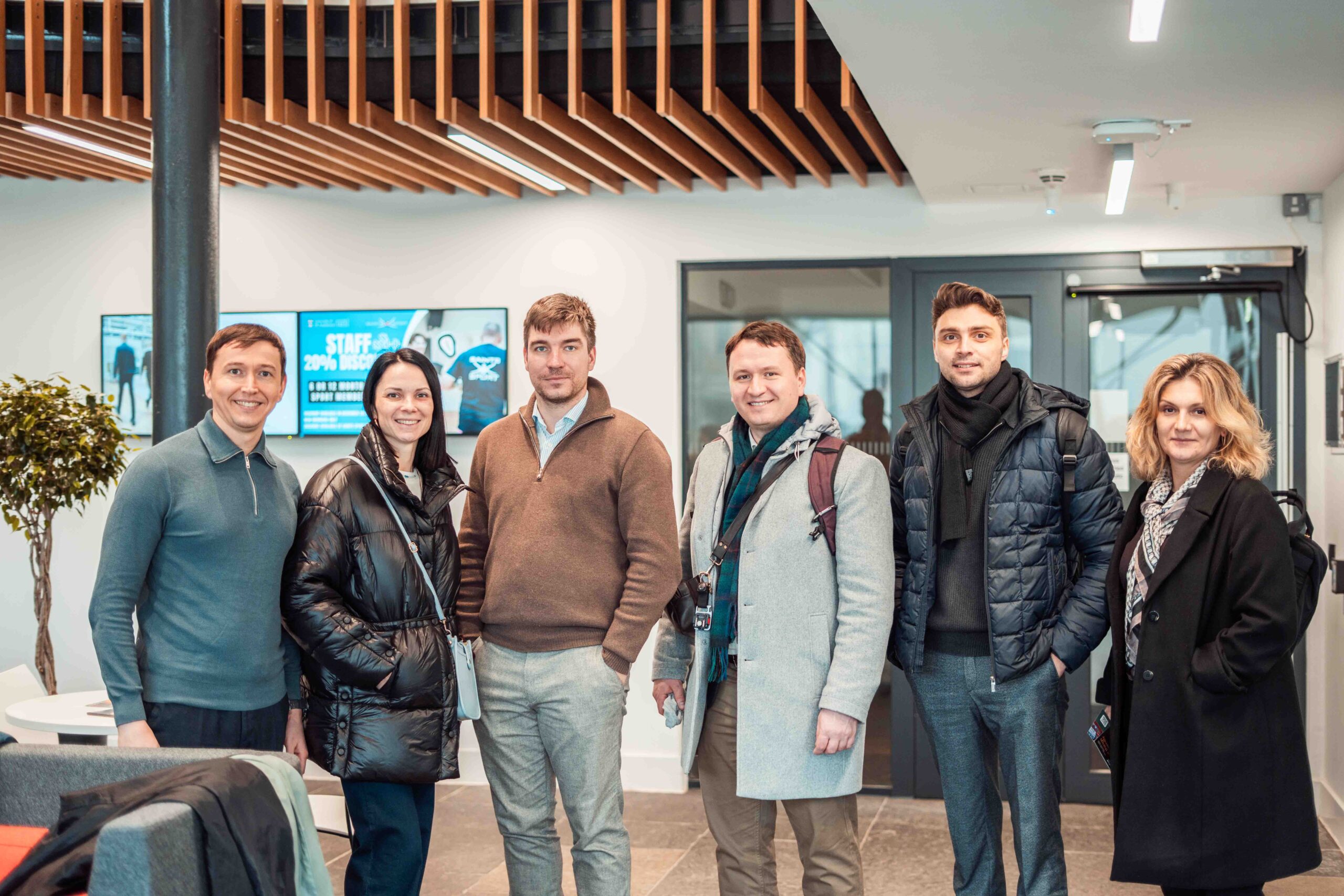 Four men and two women standing in a row in a reception of university building