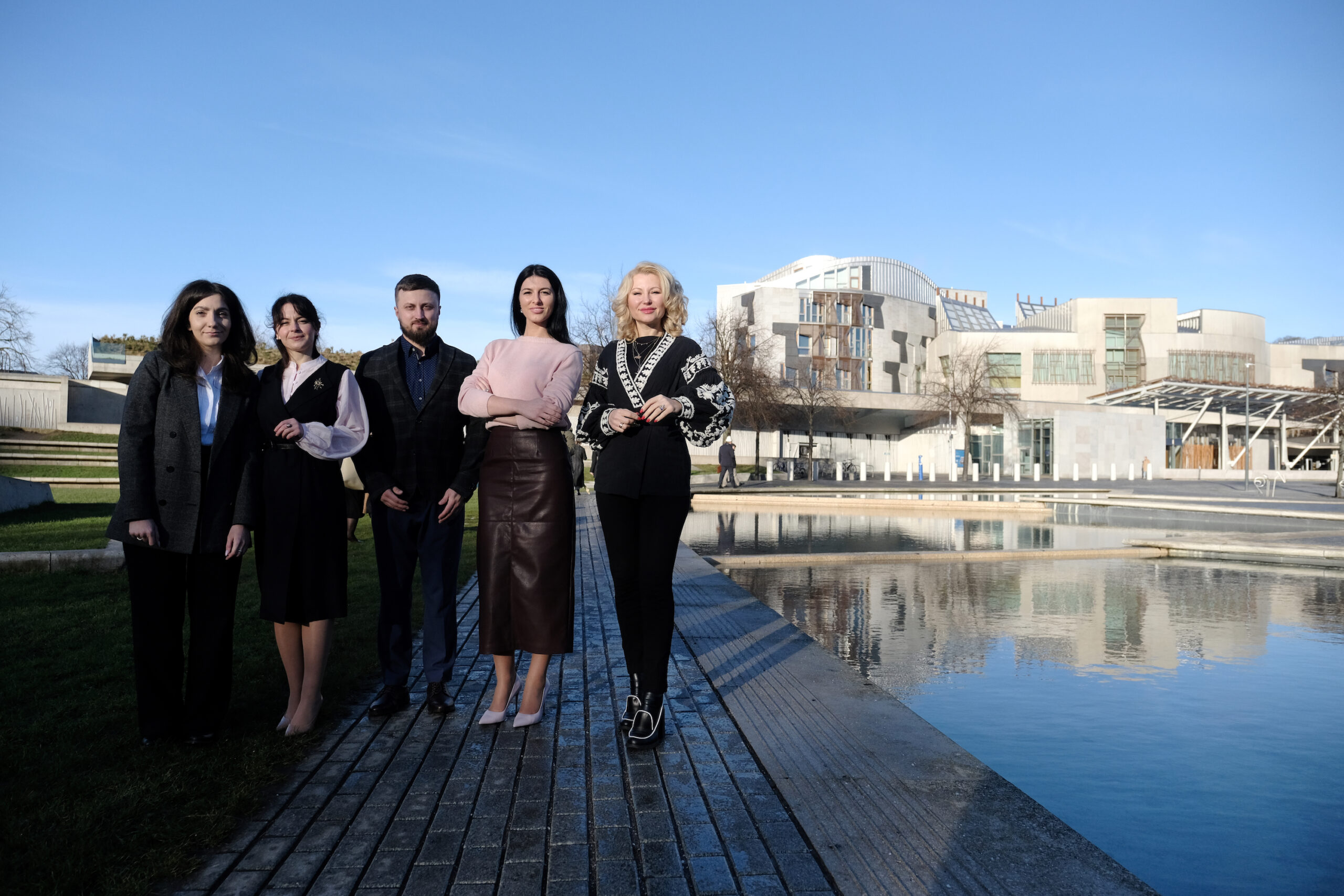 Five people standing outside building with pond in front