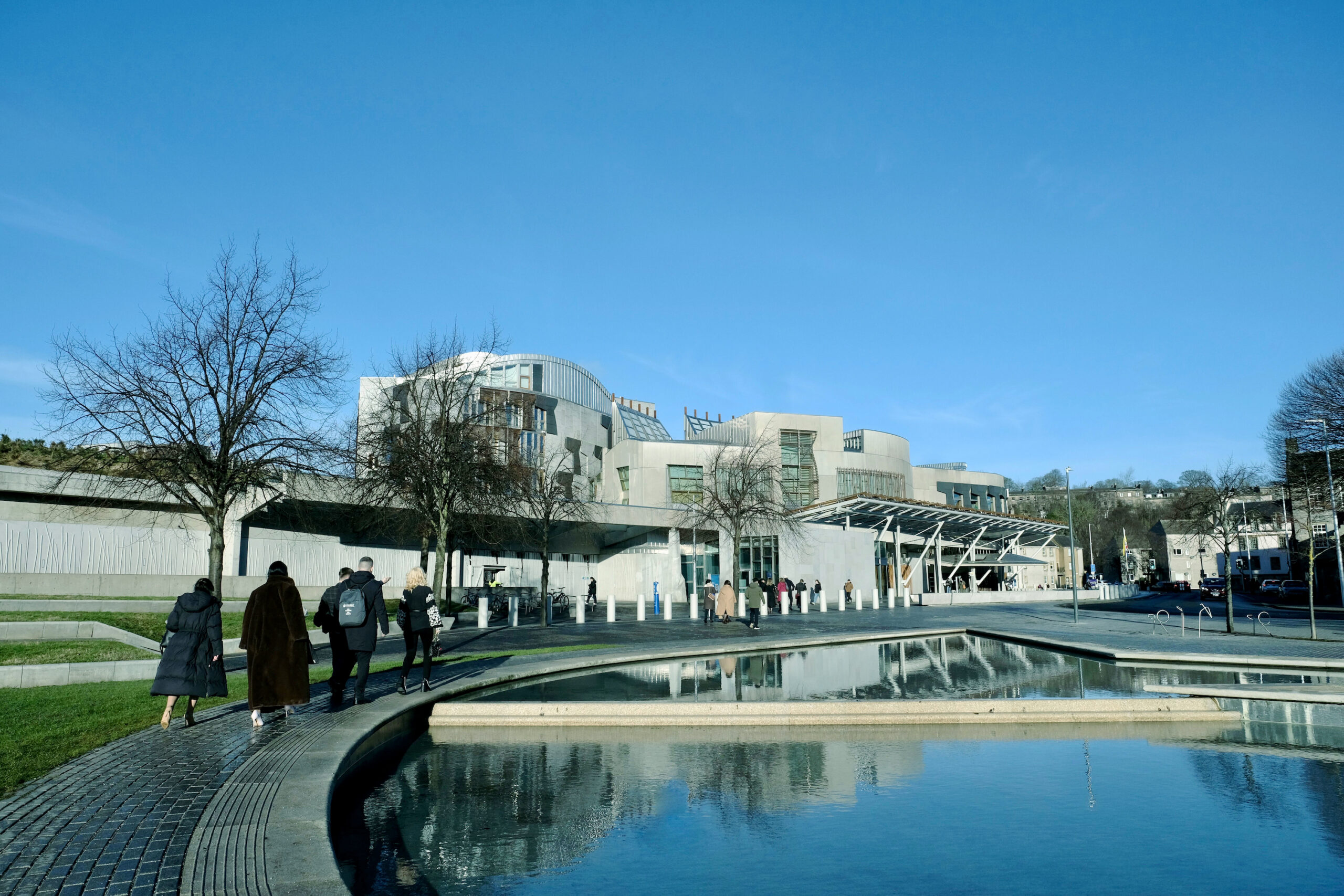 Scot parliament Fellows walking towards a building with a pond in front