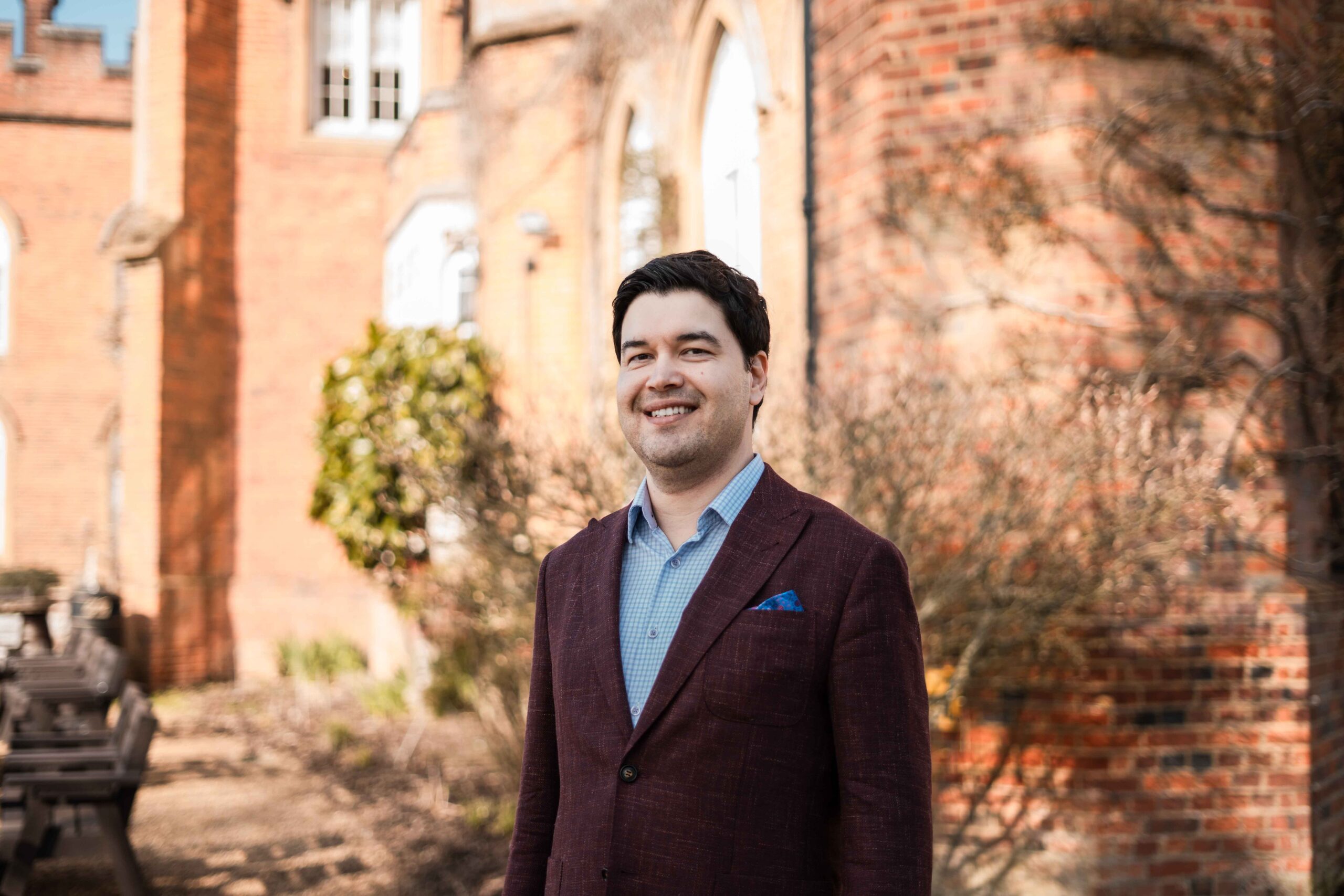 Man in a suit standing outside a large red brick manor house